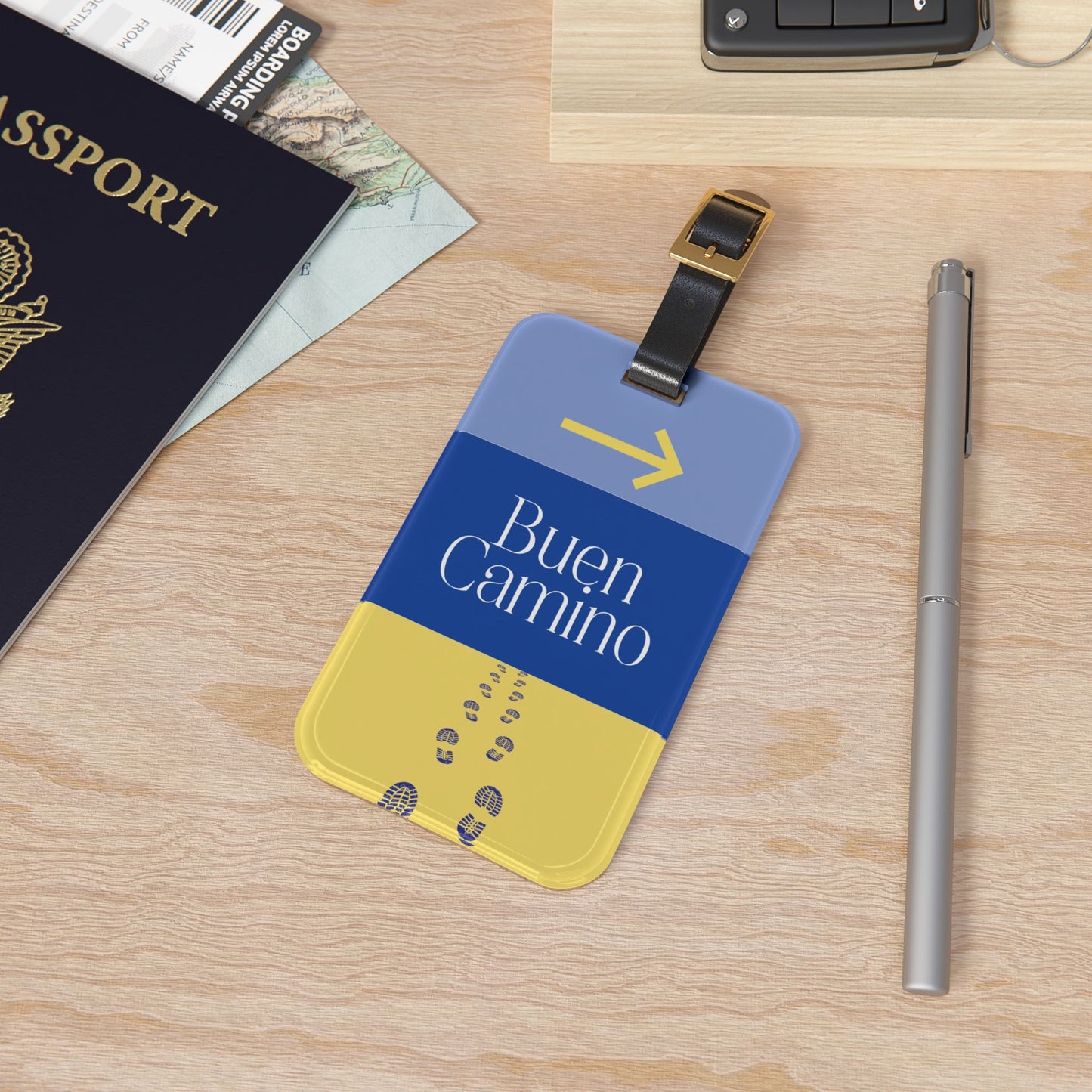 Luggage tag with 'Buen Camino' text on a wooden surface with passport and pen.