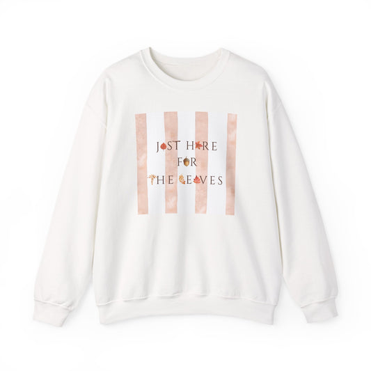 An off-white crewneck sweatshirt featuring a graphic print on the front with vertical peach stripes and the text 'JUST HERE FOR THE LEAVES' decorated with small autumn leaves.