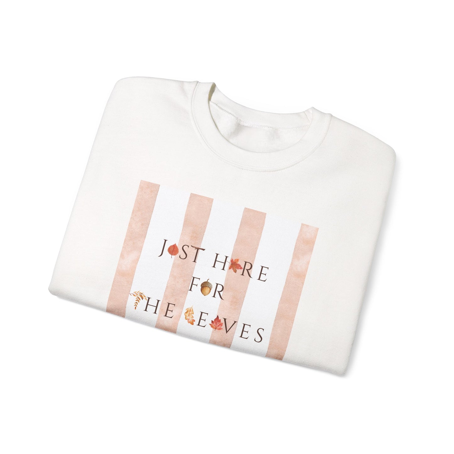 A folded white crewneck sweatshirt featuring a graphic print with vertical rose gold stripes and the text 'JUST HIDE FOR THE LEAVES' decorated with small autumn leaves, shown on a plain white background.