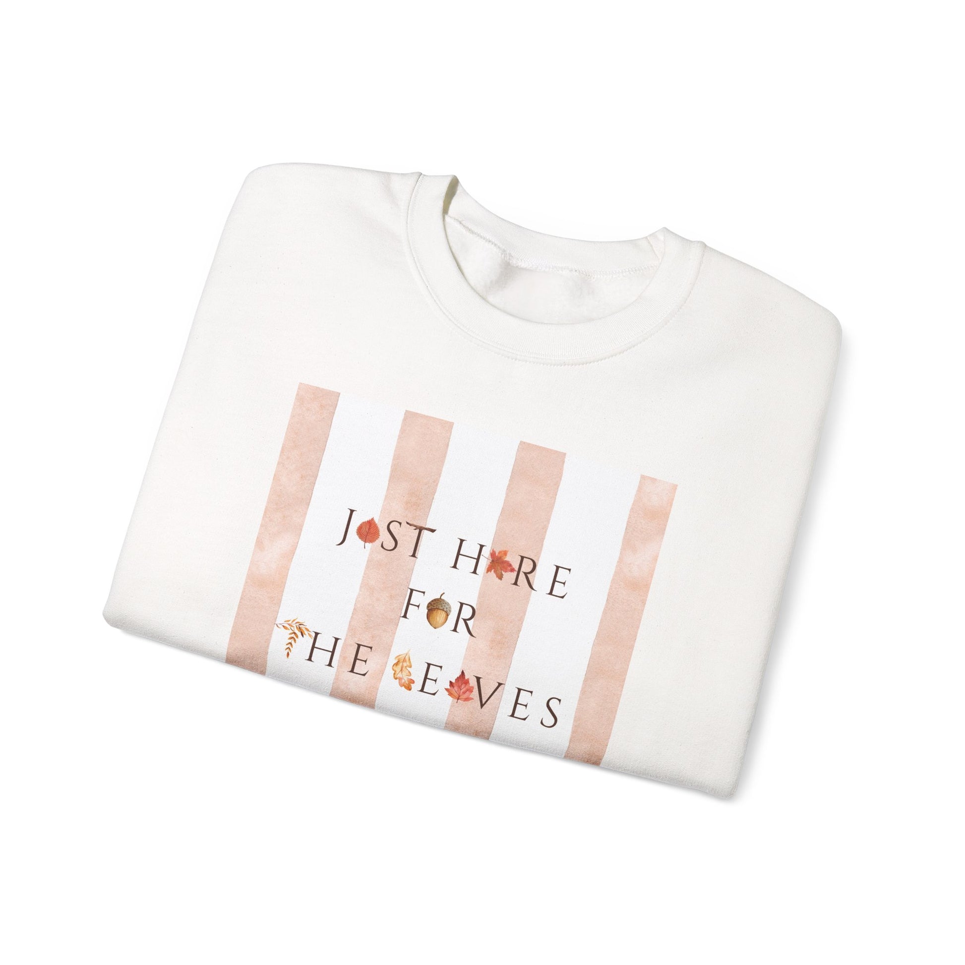 A folded white crewneck sweatshirt featuring a graphic print with vertical rose gold stripes and the text 'JUST HIDE FOR THE LEAVES' decorated with small autumn leaves, shown on a plain white background.