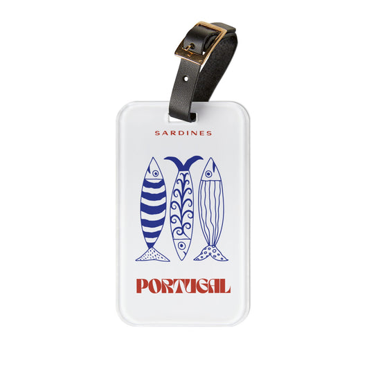 A white luggage tag with a black leather strap and gold buckle, featuring blue sardine illustrations and the words 'SARDINES' and 'PORTUGAL' in red, on a plain white background.