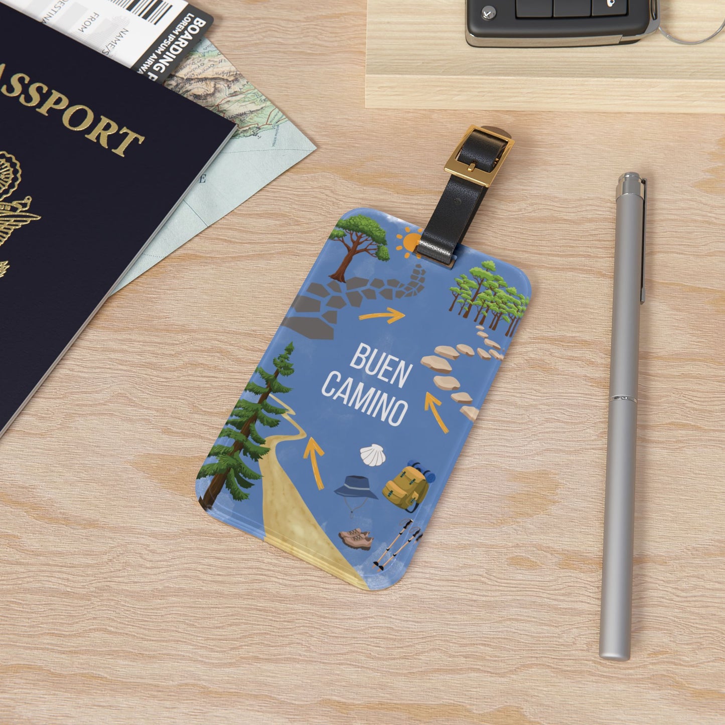 Luggage tag with 'Buen Camino' text on a wooden surface with passport and pen.