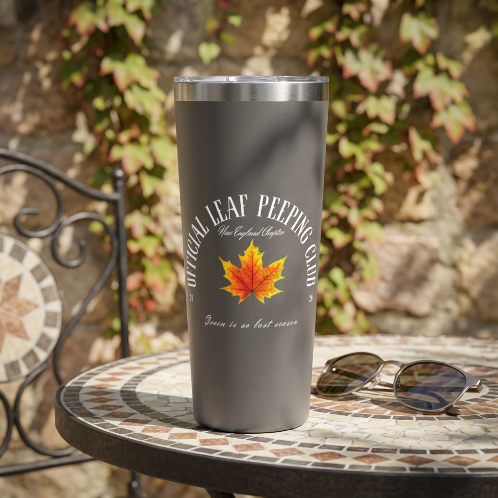 A matte dark gray insulated tumbler with a stainless steel lid sits on a mosaic outdoor table. The tumbler is printed with the phrase 'OPTICAL LEAF PEEPING CLUB', a bright orange and yellow maple leaf graphic, and 'Green is so last season'.