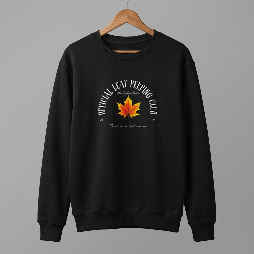 A black crewneck sweatshirt hanging on a wooden hanger against a solid gray background. The sweatshirt features a graphic print on the chest with a red and orange maple leaf in the center, surrounded by the text 'OFFICIAL LEAF WEEING CLUB' in white.