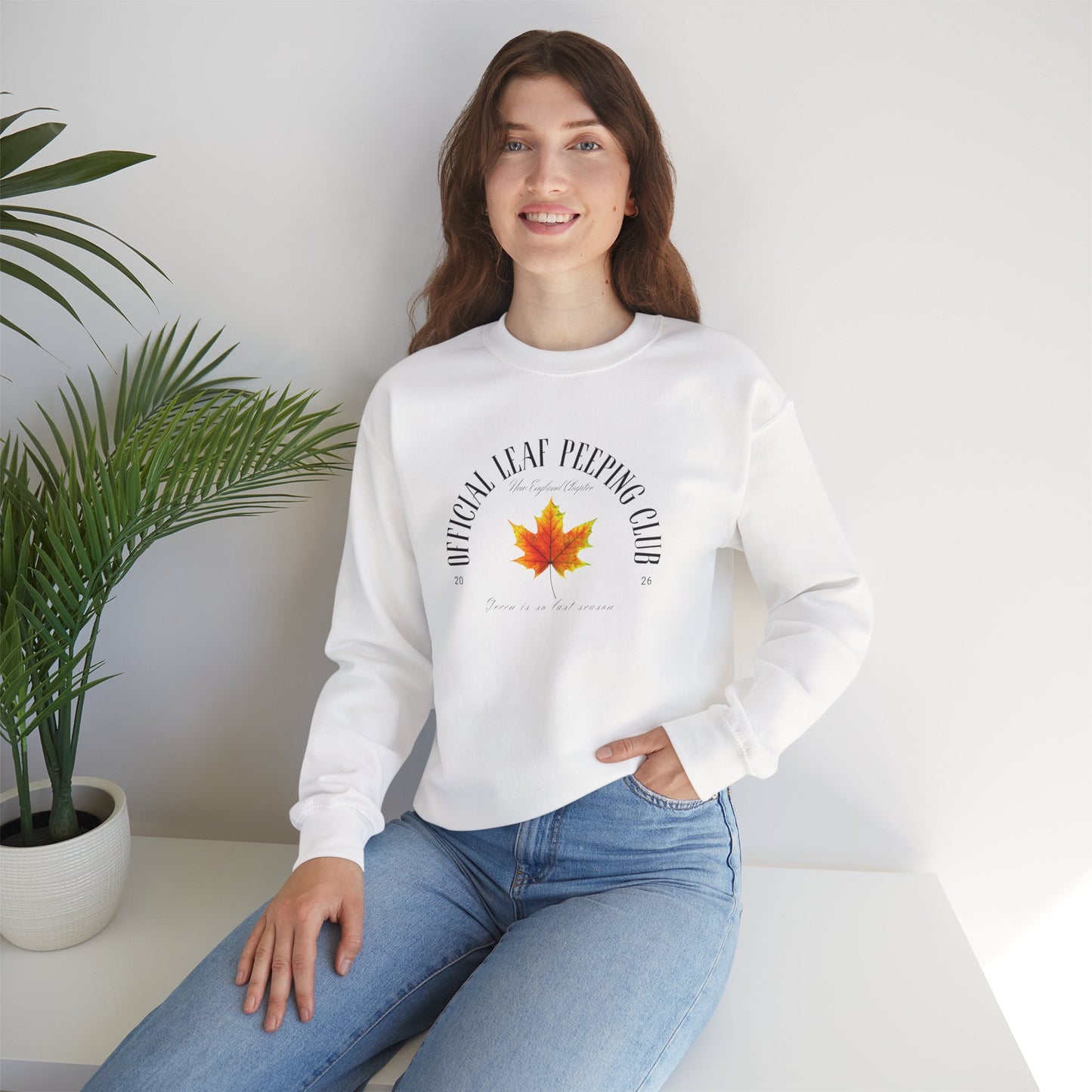 Person wearing a white sweatshirt with 'iFall leaf peeping' text, sitting in a minimalistic room.