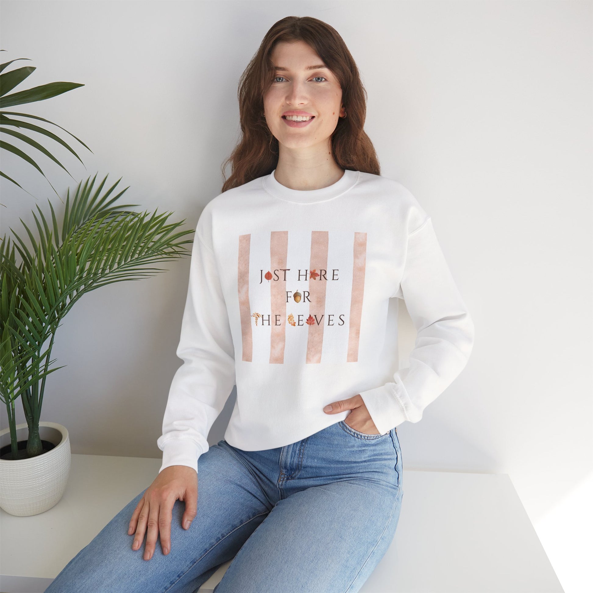 Person wearing a white sweatshirt with 'Just here for the leaves' text, sitting in a minimalistic room.